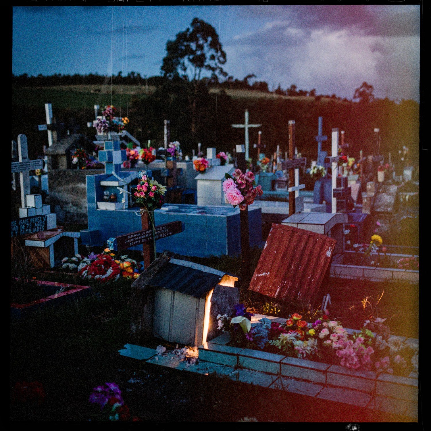 Tumbas pintadas de azul y rojo con cruces y flores en el cementerio de Apiao