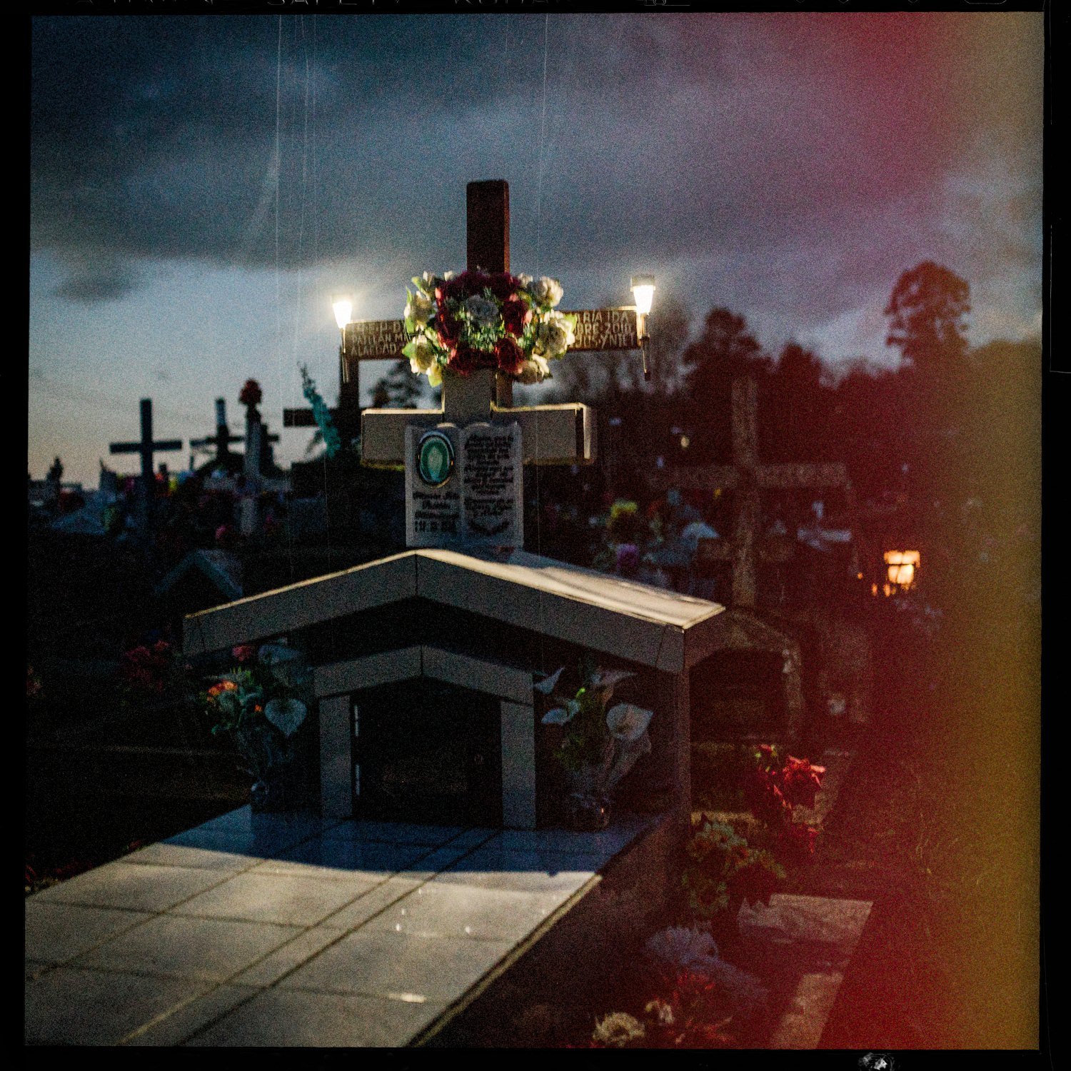 Tumba con cruz, flores y velas encendidas en el cementerio de Apiao, al anochecer