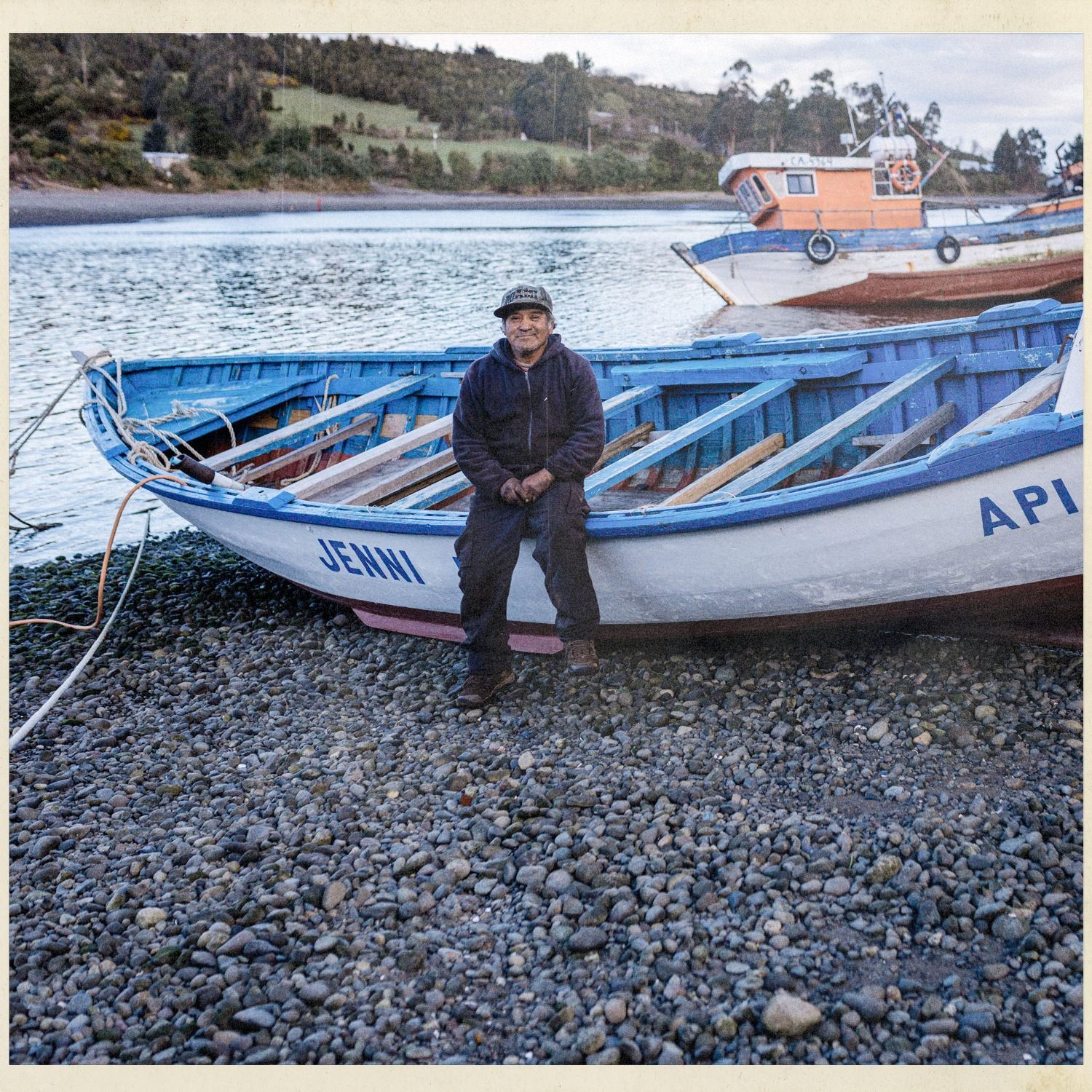 Don Juan sentado junto a un bote de madera en la playa de Apiao