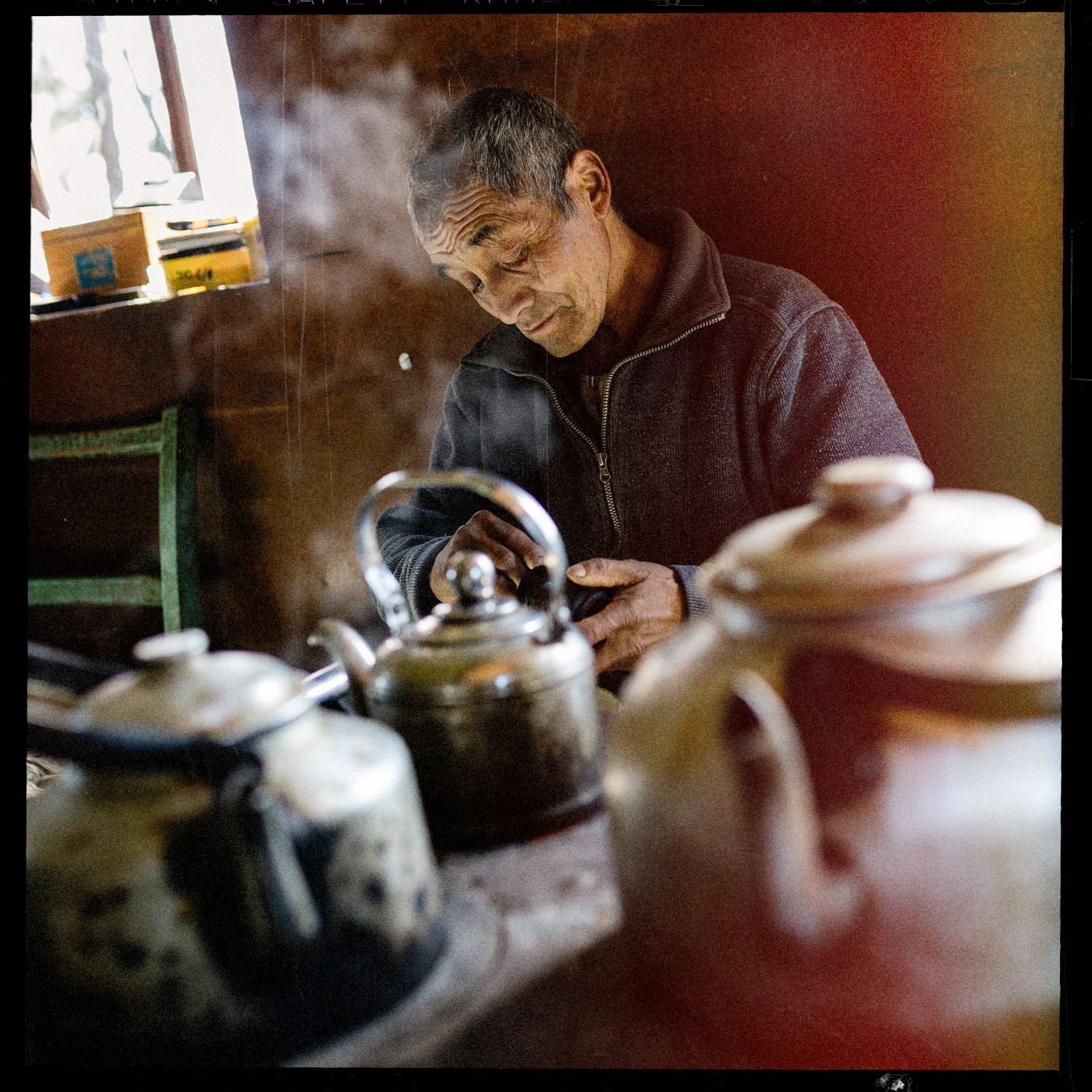 Hombre junto a una cocina a leña con teteras, en una casa de Apiao