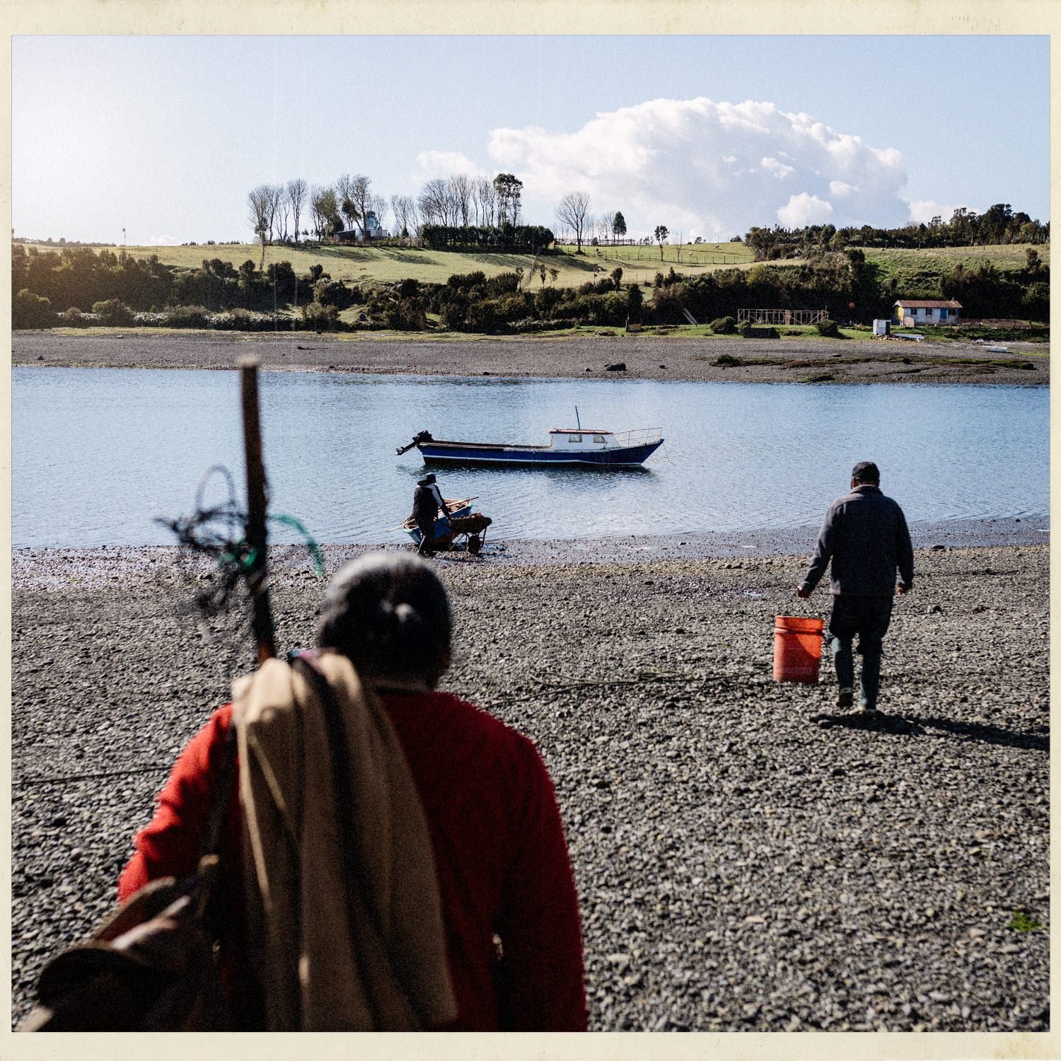 Personas caminando por la playa de Apiao hacia un bote, con el campo al fondo