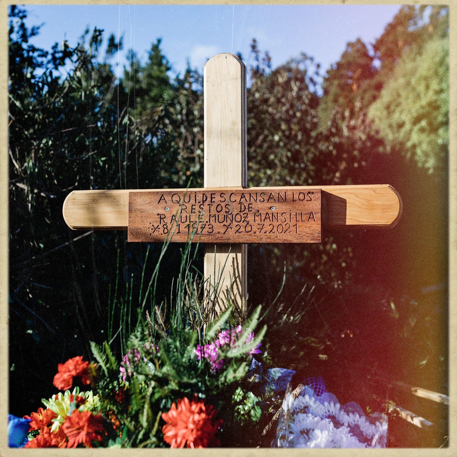 Cruz de madera con una placa y flores de colores, en memoria de un difunto