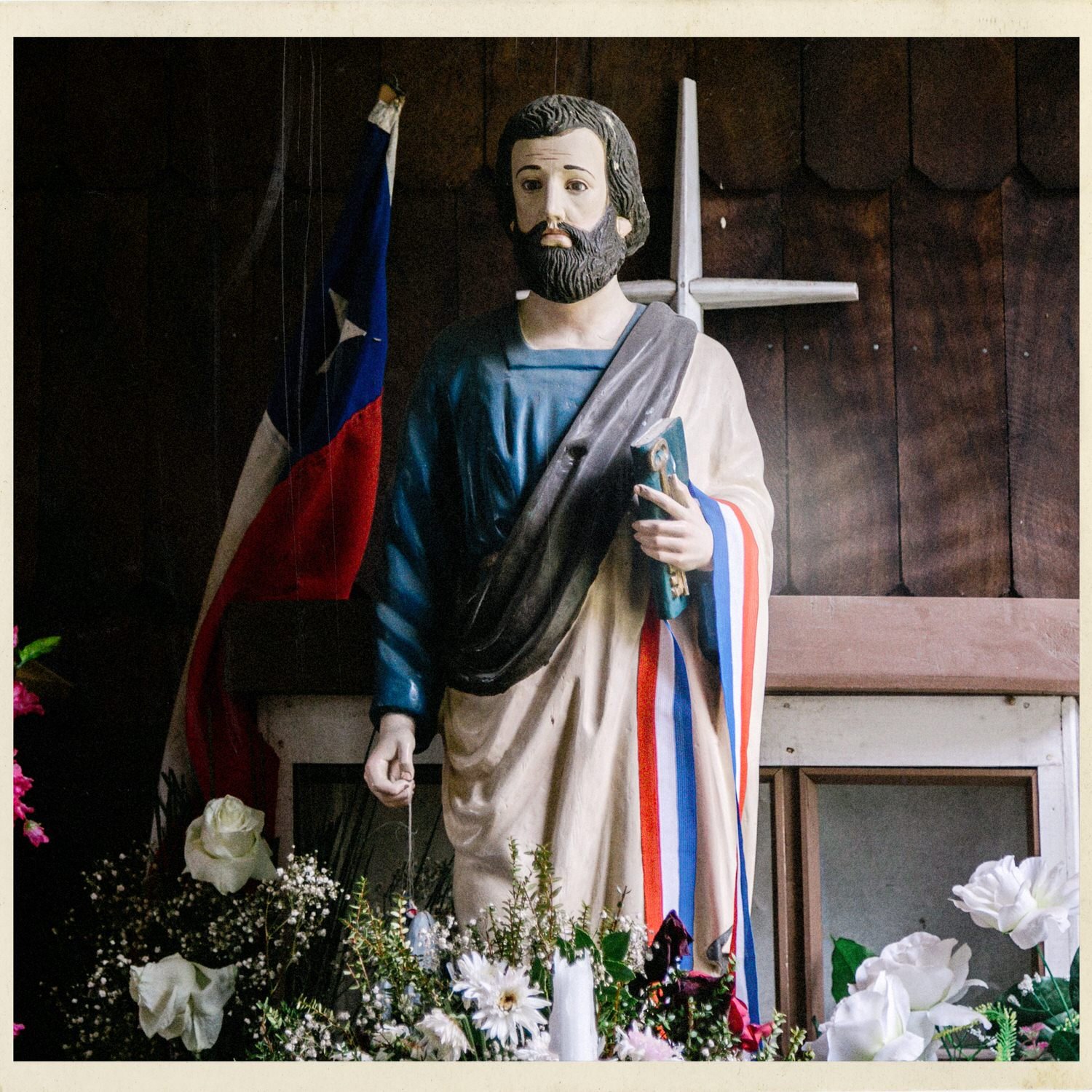 Imagen religiosa de un santo con una bandera chilena y flores, en la iglesia de Caulín