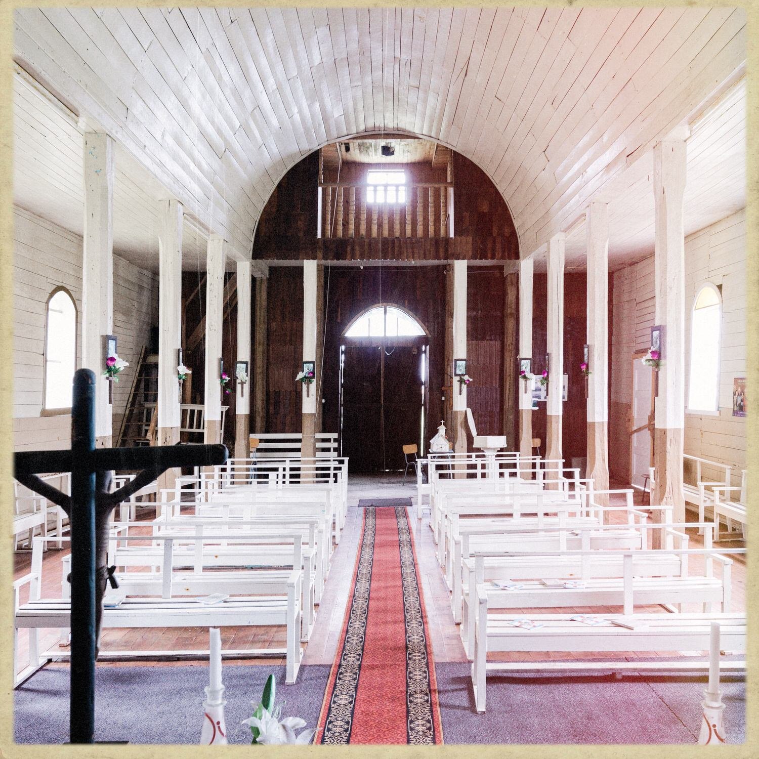 Interior de la iglesia de Caulín: nave central, bancas blancas y un crucifijo