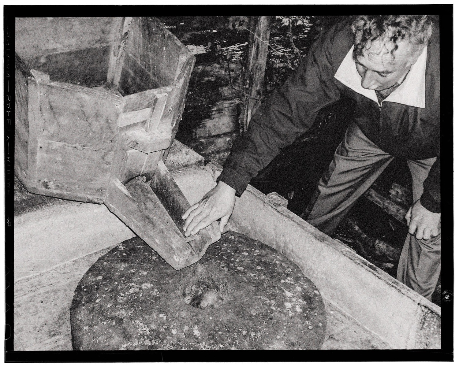 Don Bernardo trabaja junto a una piedra de molino, en blanco y negro
