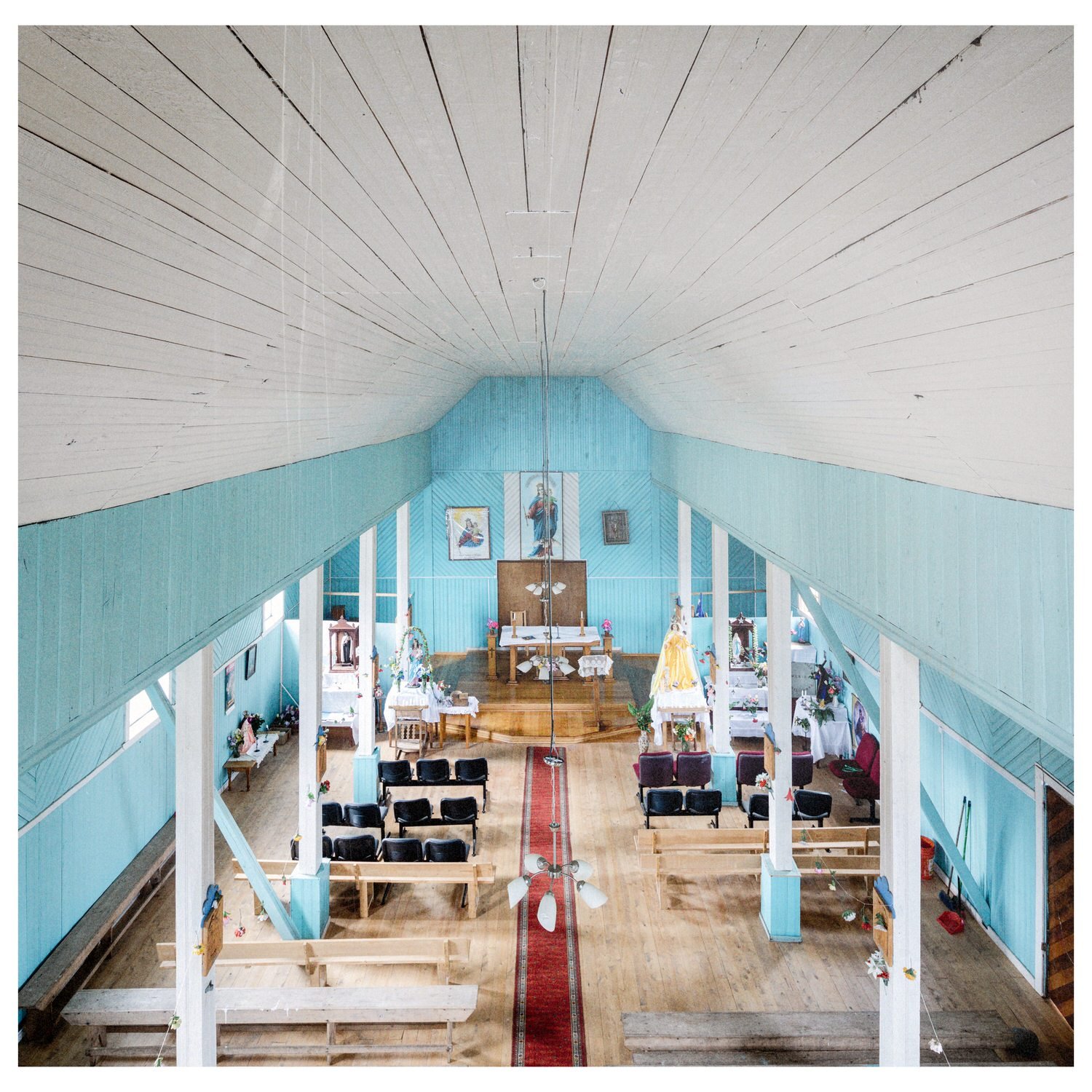 Nave de la iglesia de Chullec con muros celestes, cielo blanco y alfombra roja