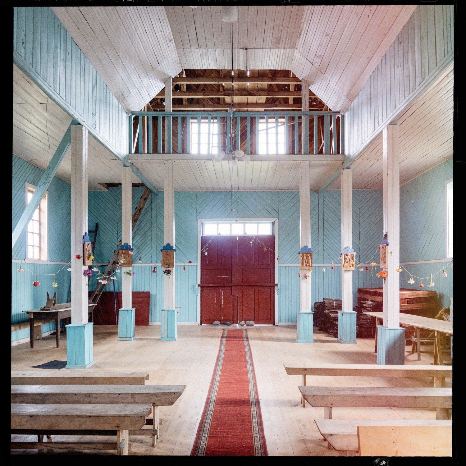 Interior de la iglesia de Chullec hacia la entrada, con el coro en altura y la puerta roja