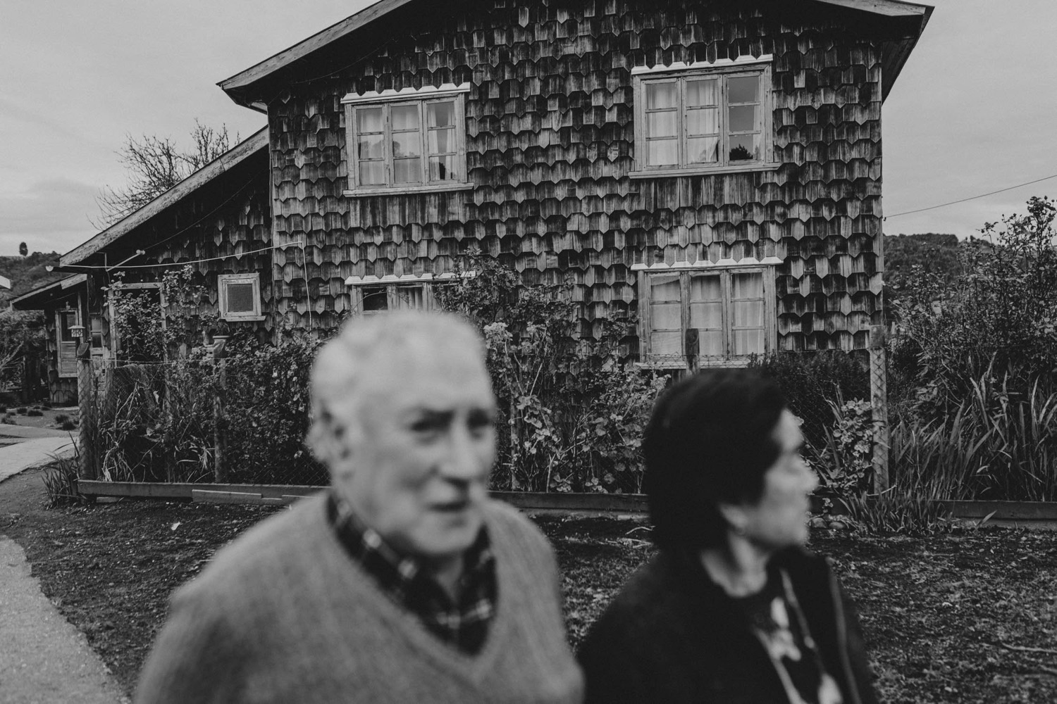 Doña Berta y don Bernardo frente a una casa de tejuelas, en blanco y negro