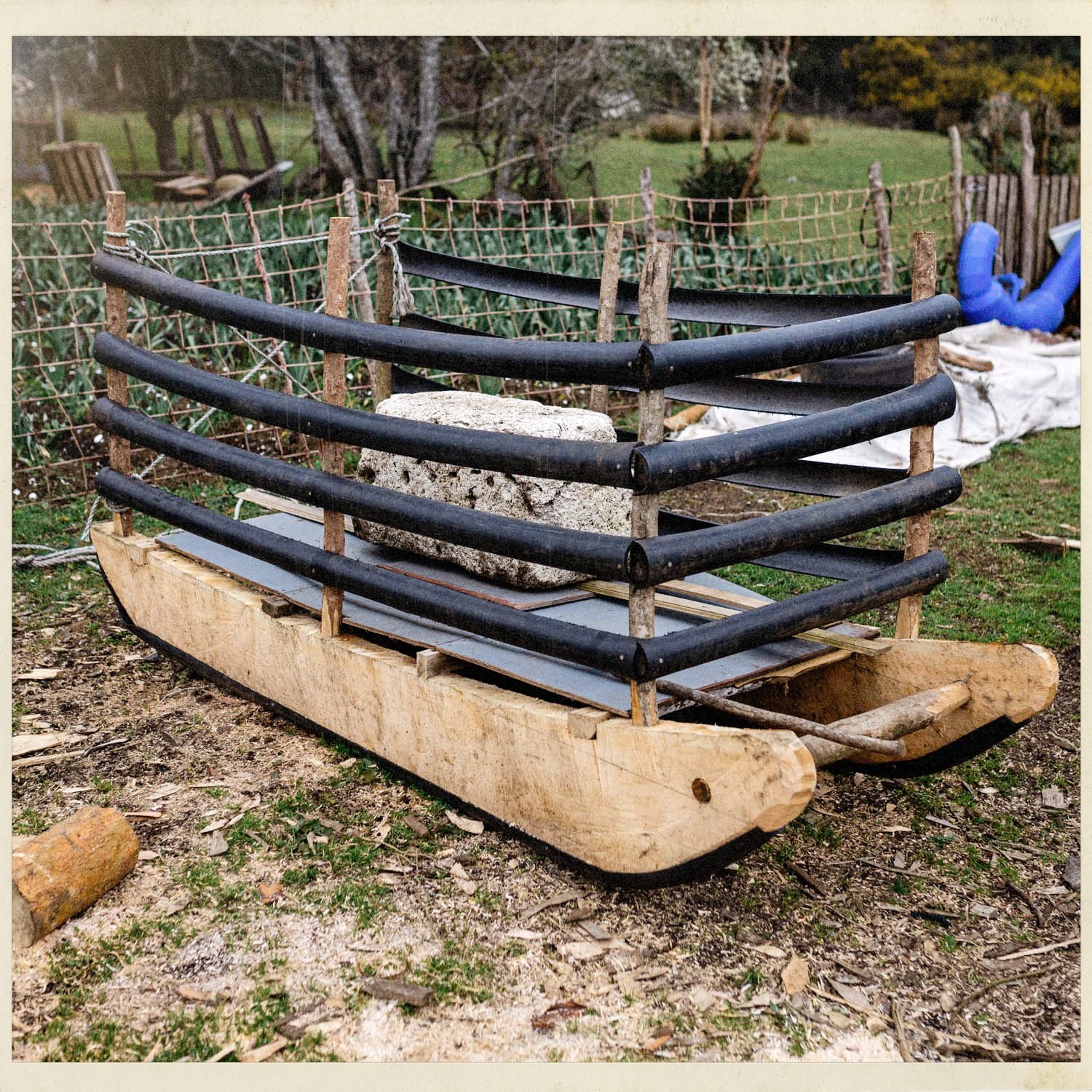 Estructura de madera con tubos negros sobre una base de tronco, en un patio de Compu