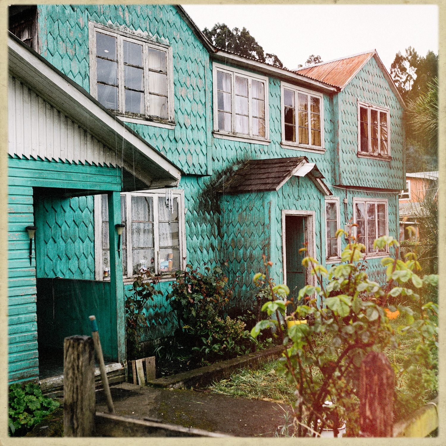 Casa de tejuelas pintada de verde agua, con su jardín, en Llingua