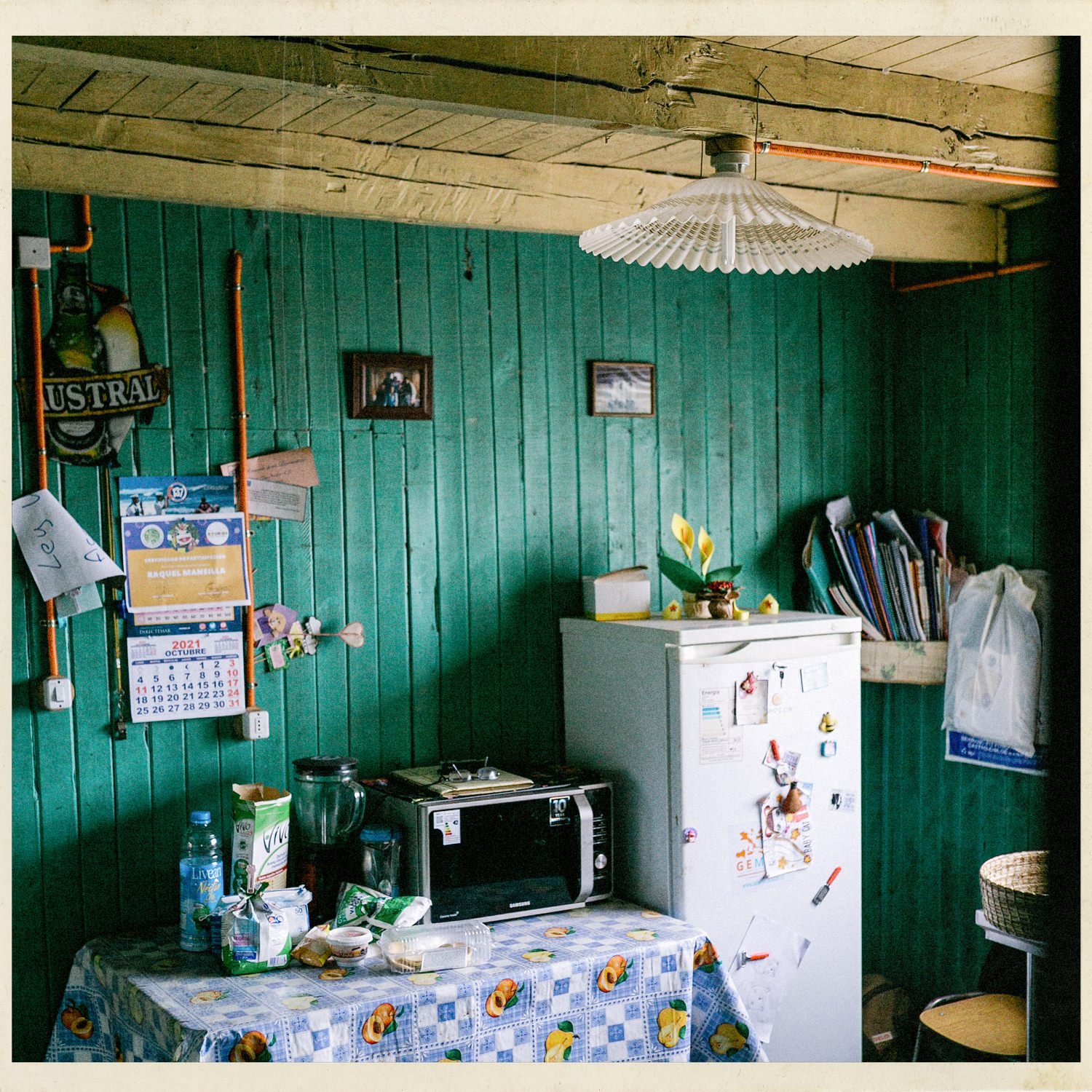 Cocina de muros verdes con refrigerador, mesa y un calendario, en Llingua