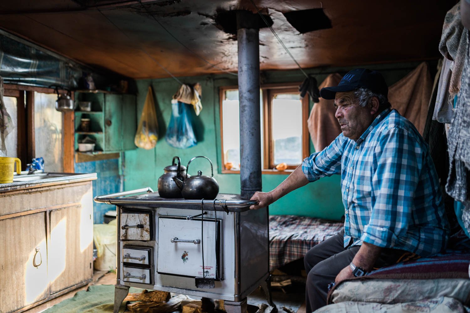 Don Humberto sentado junto a la cocina a leña de su casa, en Llingua