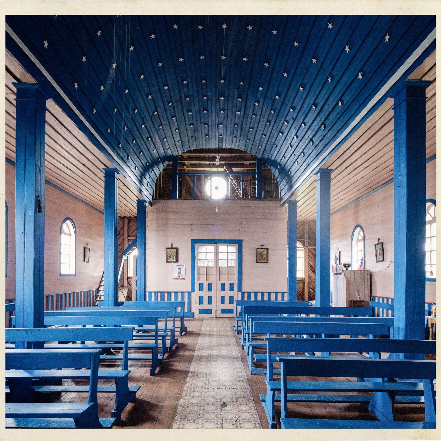 Interior de la iglesia de Llingua hacia la entrada, con el coro y bancas azules