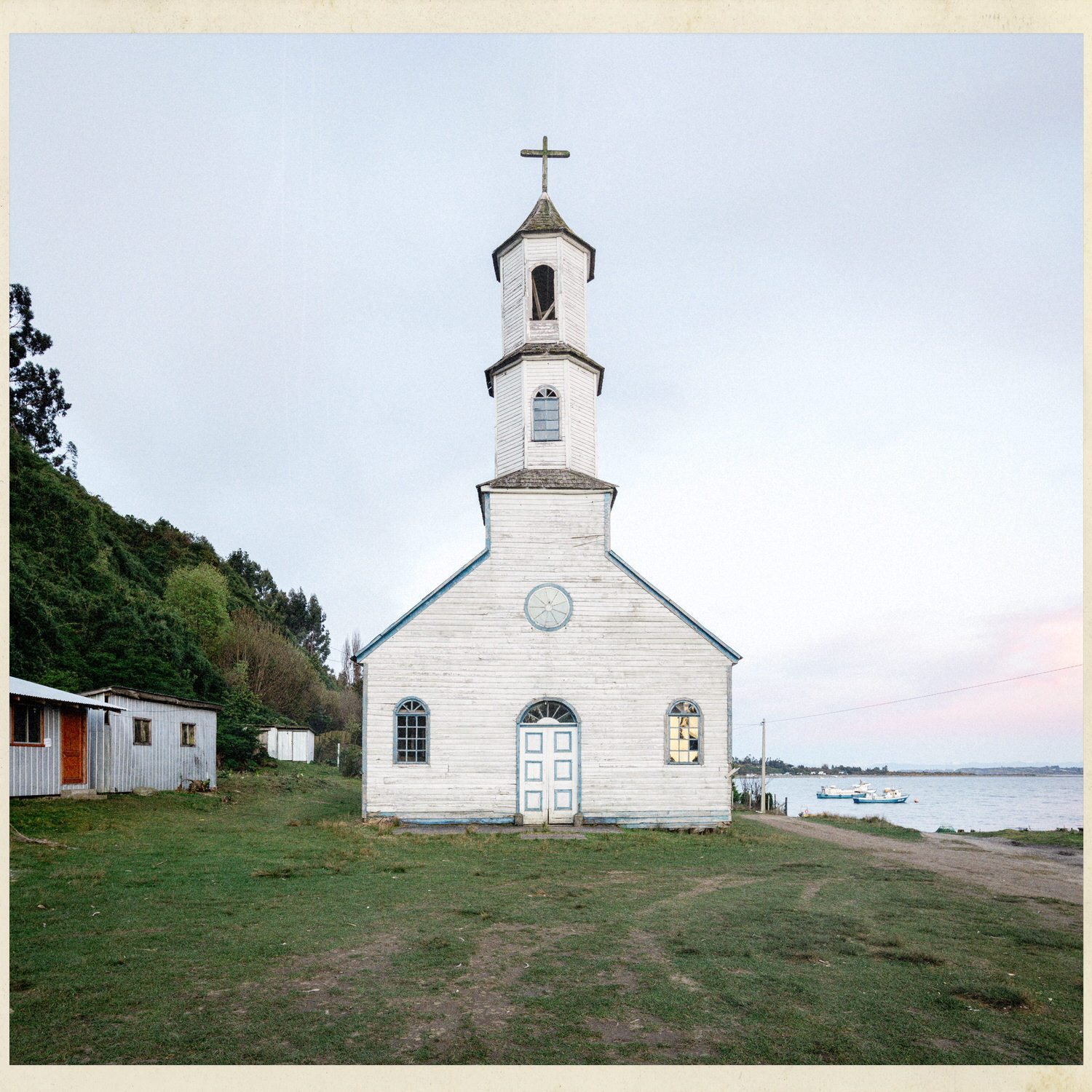 Fachada blanca de la iglesia de Llingua con su torre, frente al mar