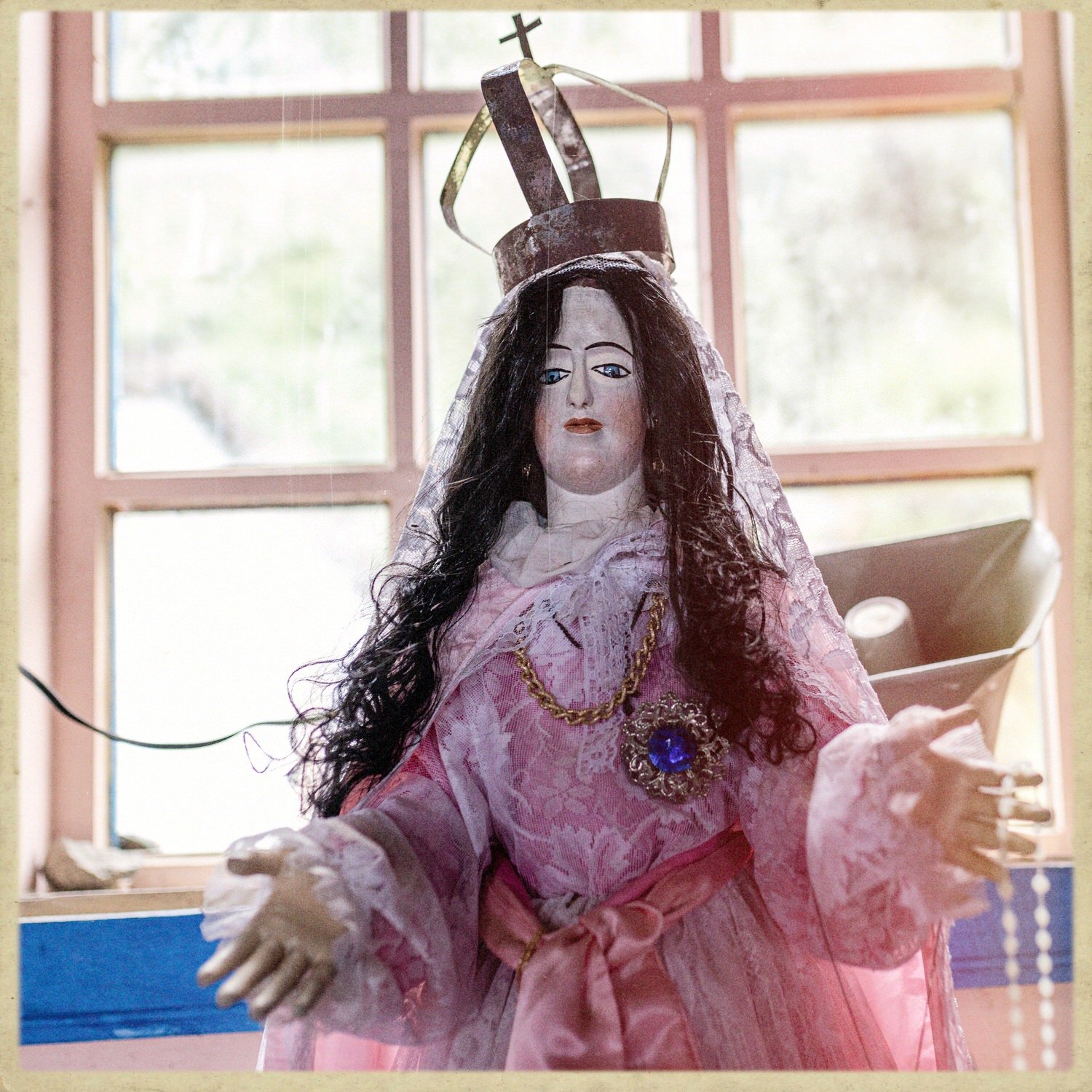 Imagen de la Virgen con corona y vestido rosado, junto a una ventana, en la iglesia de Llingua