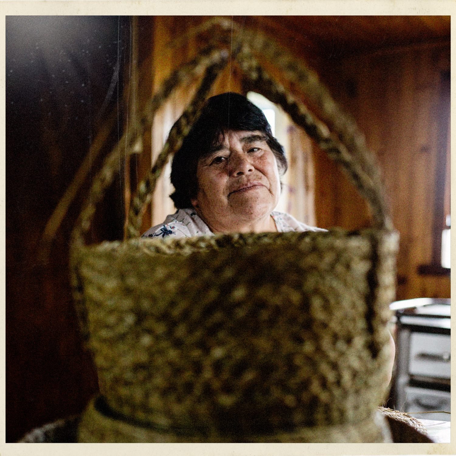 Doña Irene sonríe detrás de un canasto tejido, en su casa de Llingua