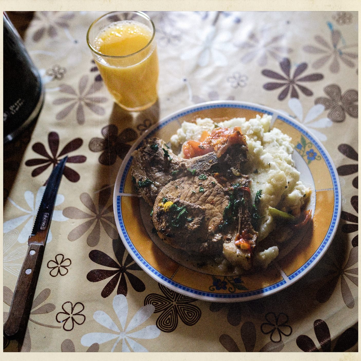 Plato de almuerzo con carne y puré, y un vaso de jugo, sobre un mantel de flores