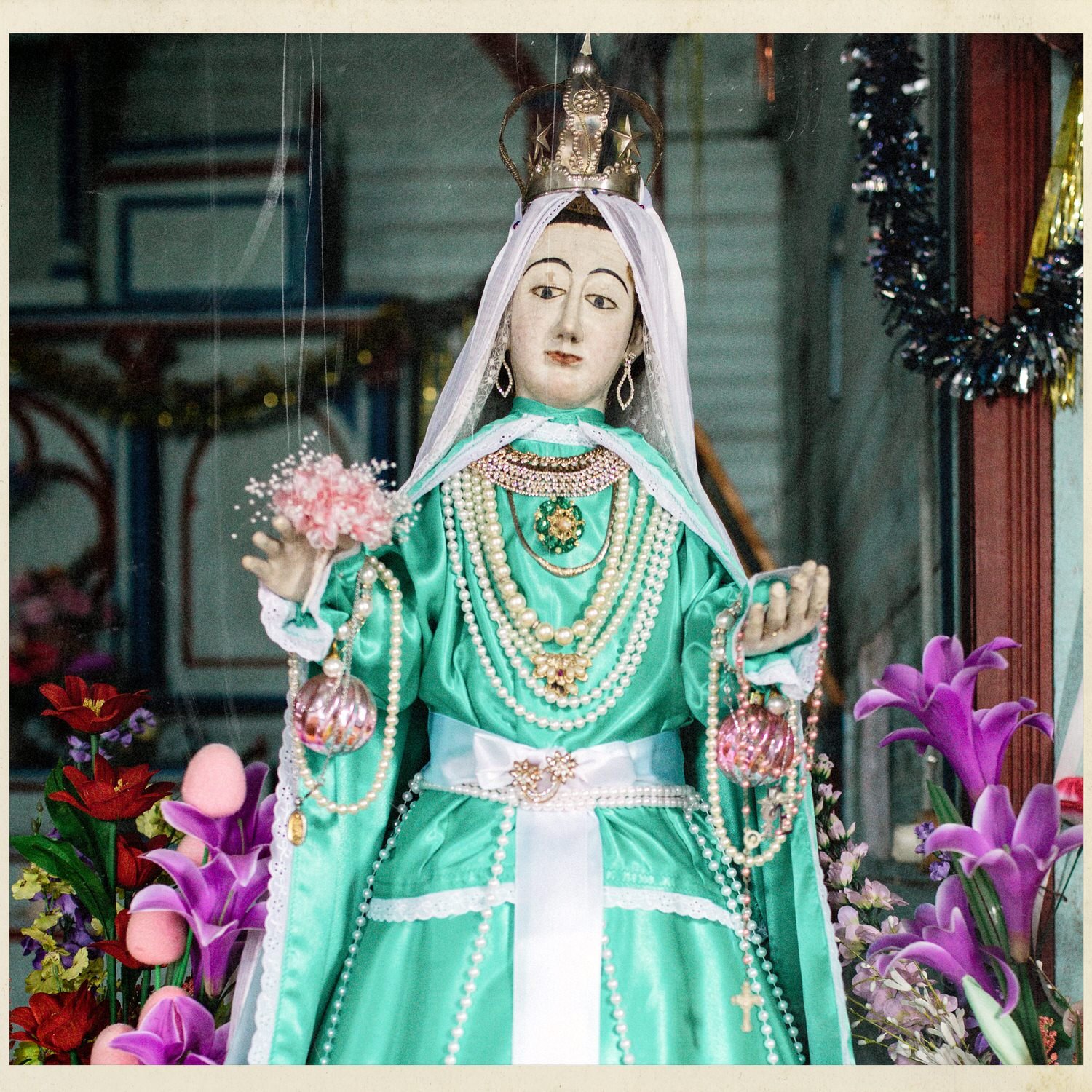 Imagen de la Virgen con manto verde y collares, entre flores, en la iglesia de Matao
