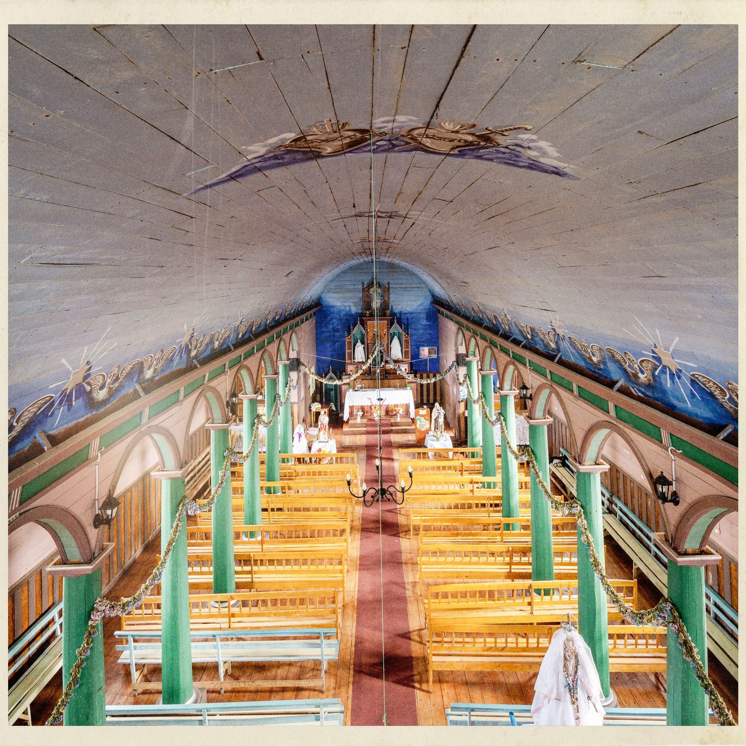 Nave de la iglesia de Puchilco con bóveda pintada, columnas verdes y bancas