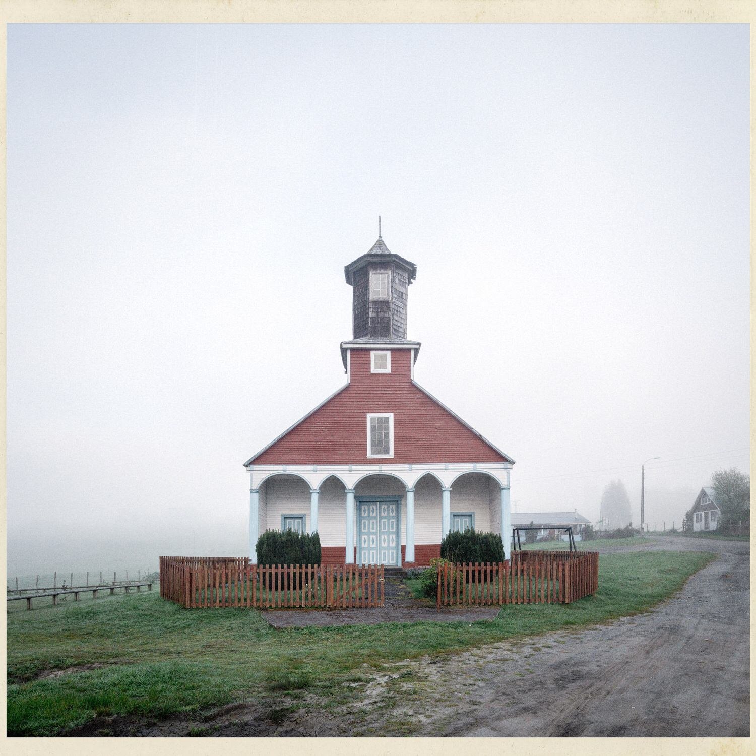 Fachada de la iglesia de Puchilco con techo rojo y pórtico blanco, en la neblina