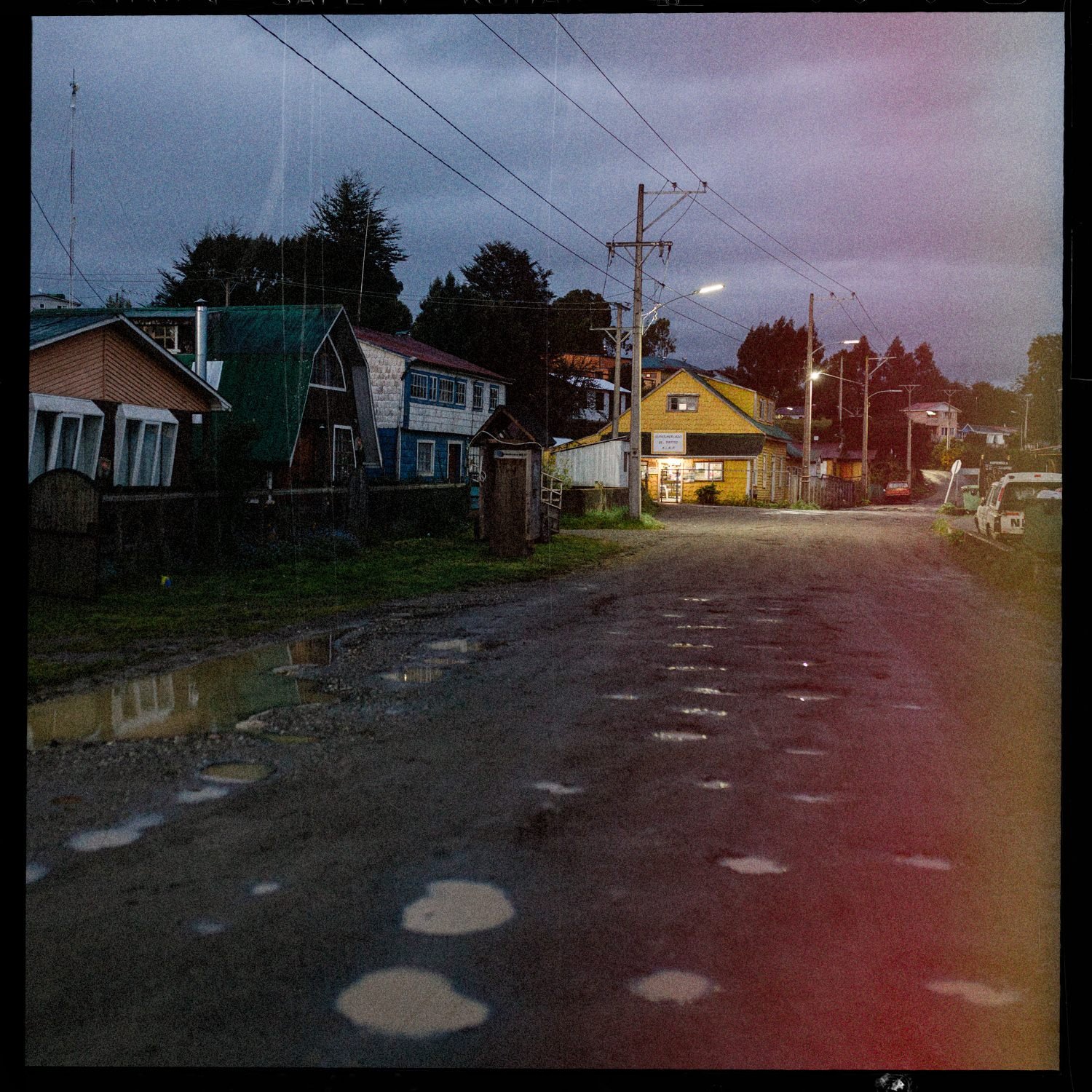 Calle del pueblo de Quehui al anochecer, con casas y postes de luz