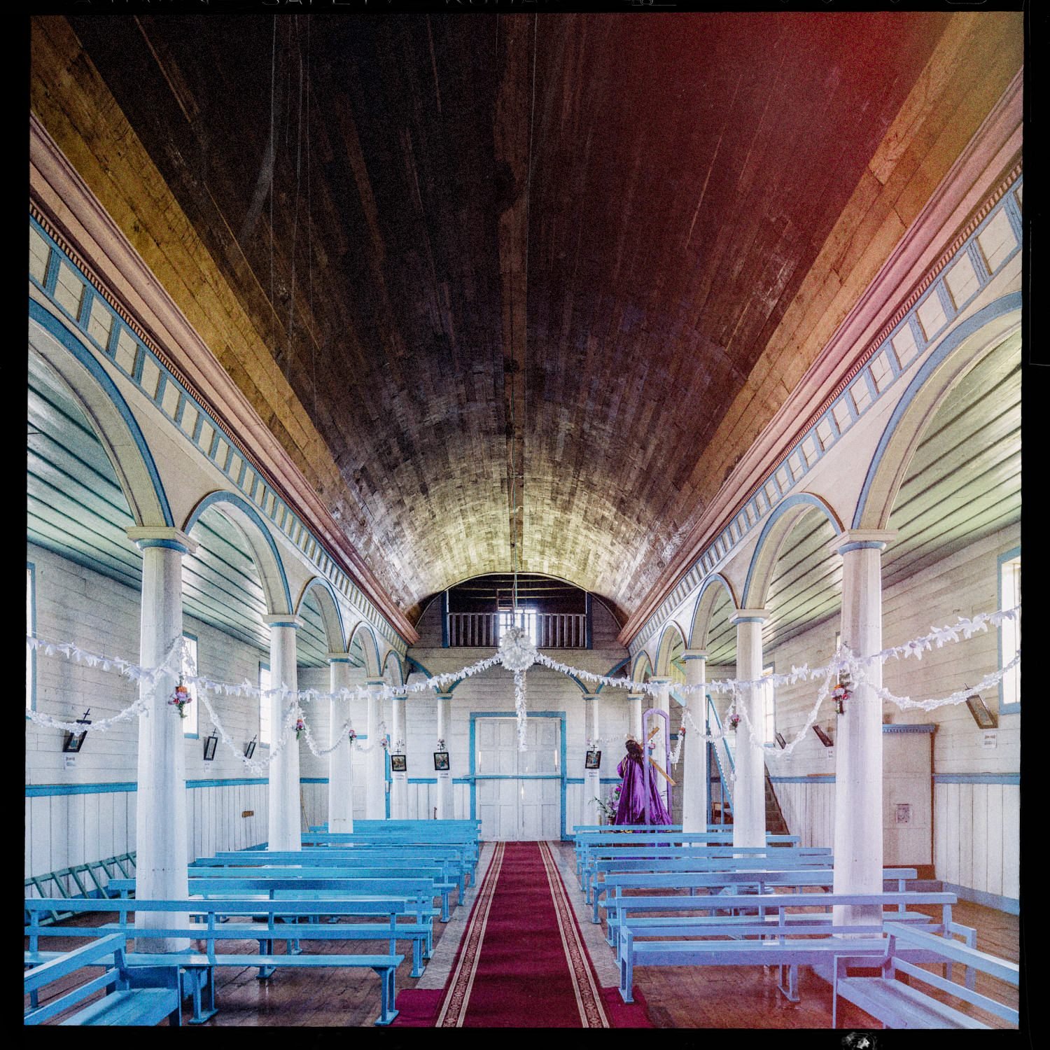 Nave de la iglesia de Quehui con bóveda de madera, columnas blancas y bancas celestes