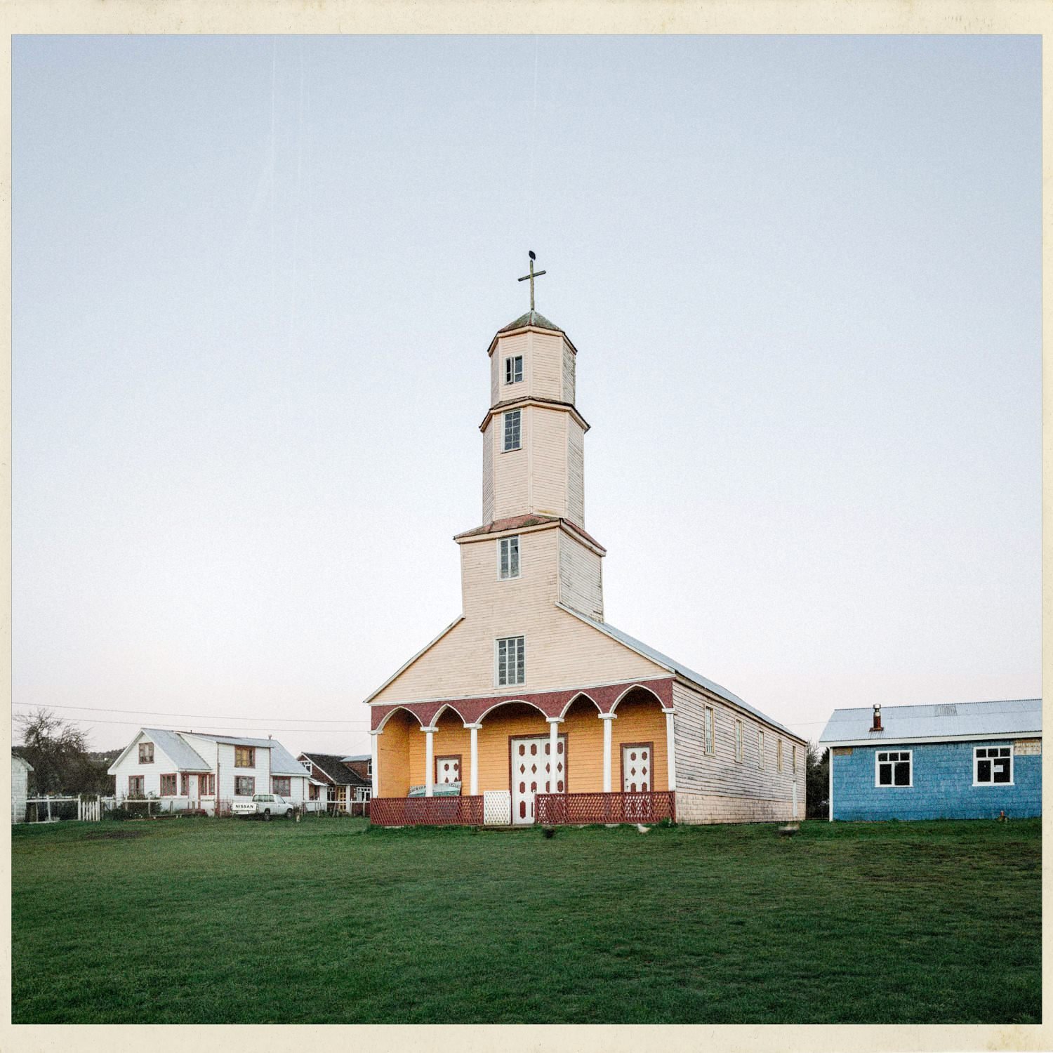 Fachada de la iglesia de Quehui con su torre alta y pórtico amarillo