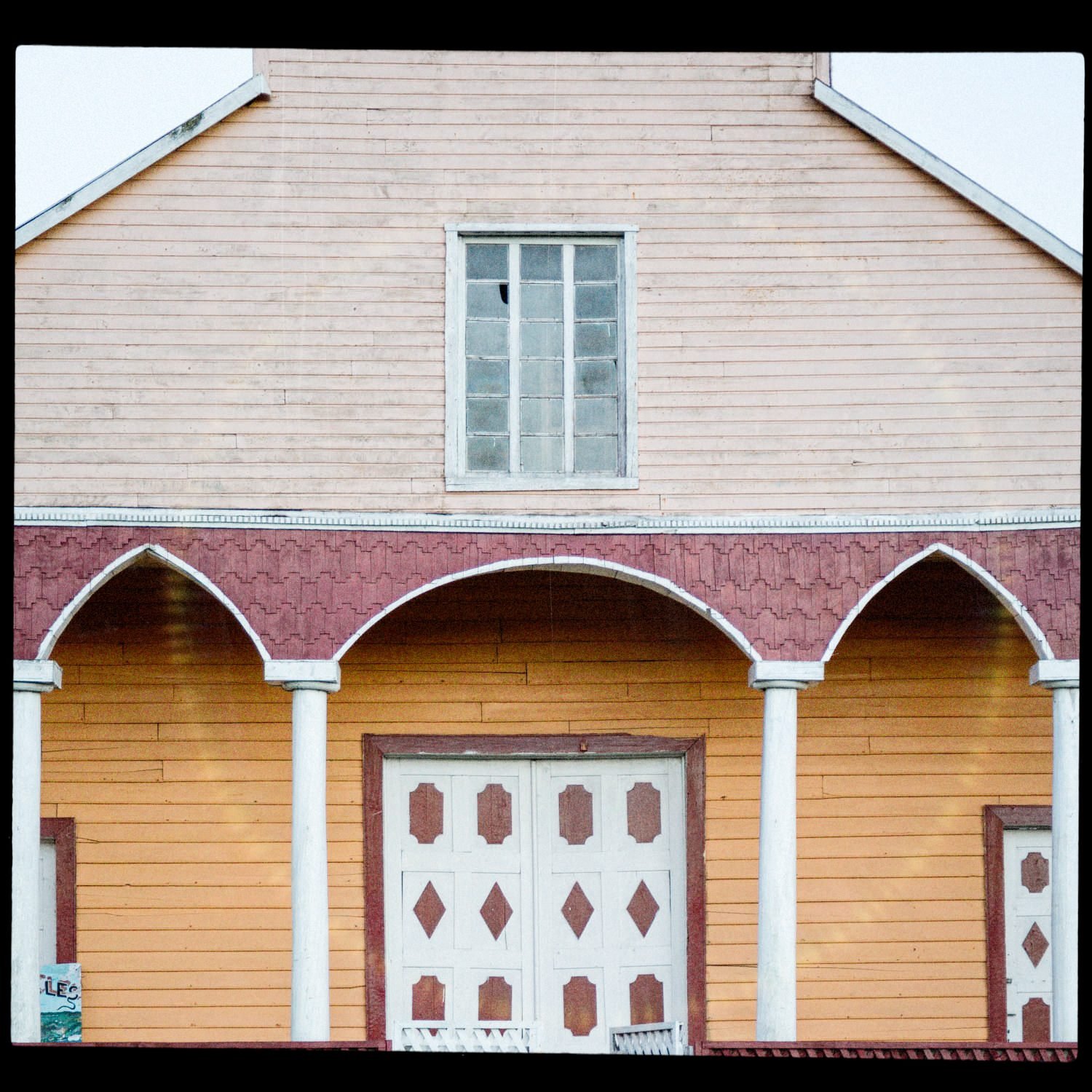 Pórtico amarillo con arcos y puerta blanca, en la iglesia de Quehui