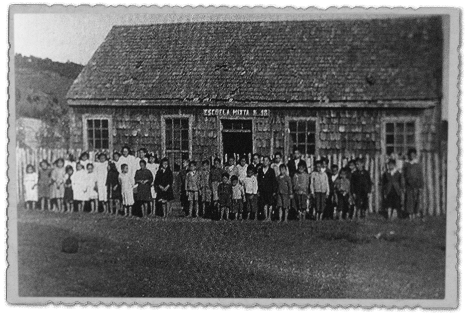 Fotografía antigua de un grupo de personas frente a una escuela de tejuelas