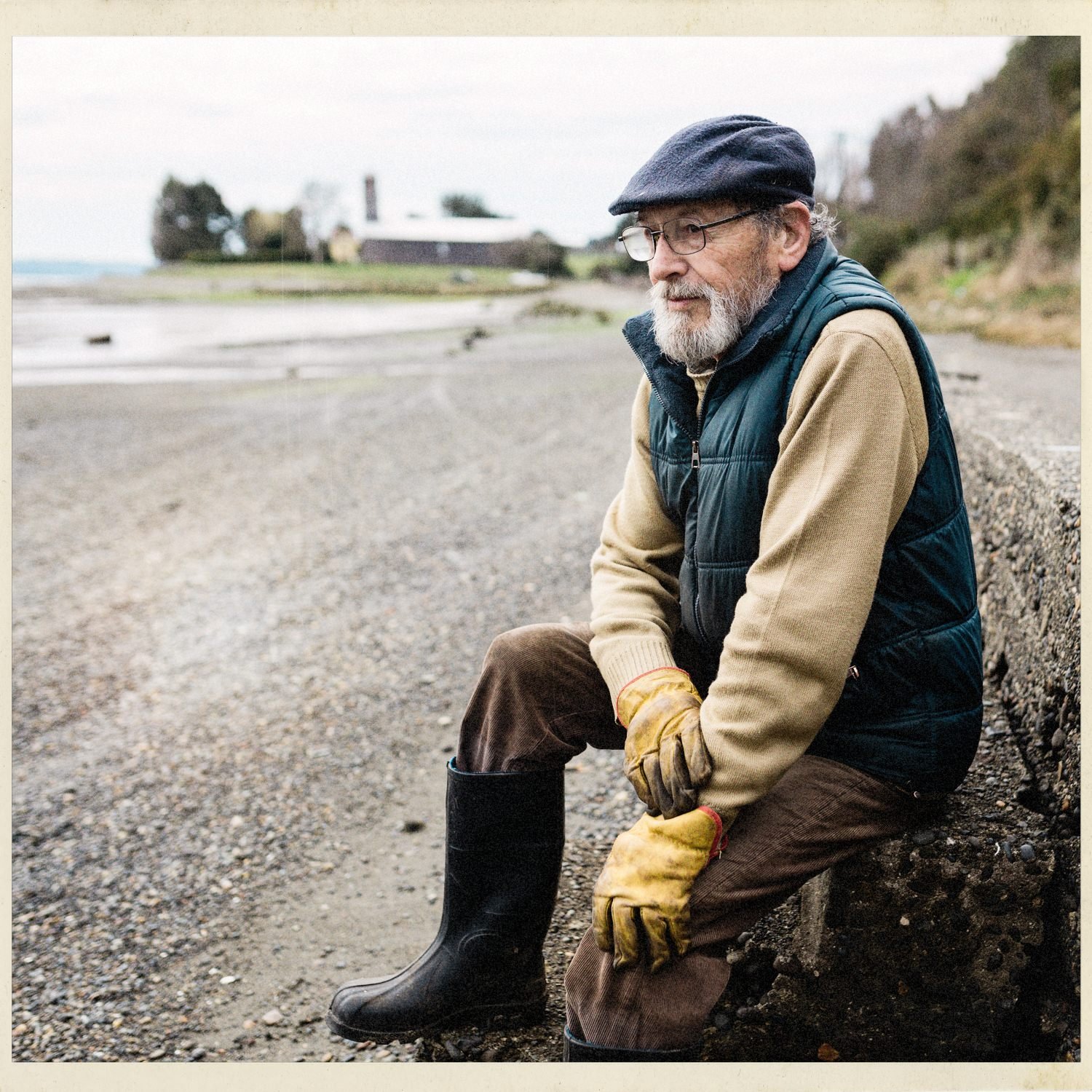 Don Tino, con boina y guantes, sentado junto a la playa de San Javier