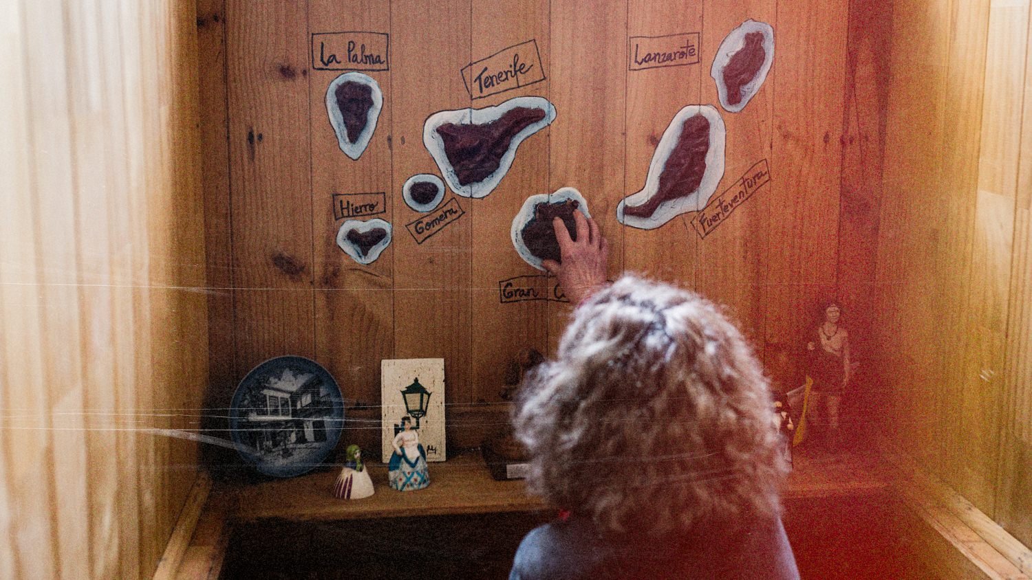 Maribel señala el mapa de las islas Canarias pegado en una pared de madera
