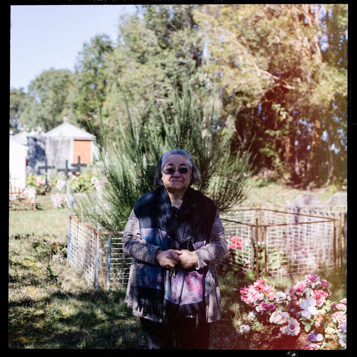 Doña Tita de pie entre flores en el cementerio de Teupa