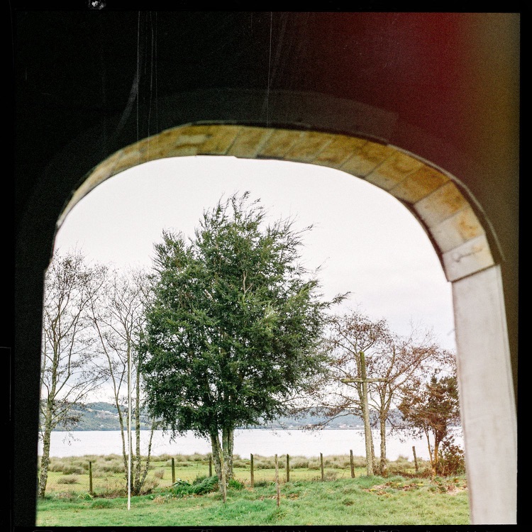 Vista de un paisaje con árboles y un lago, vista a través de un arco en un edificio con paredes de ladrillo y estructura de piedra.