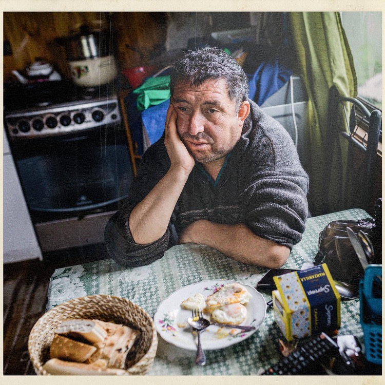 Don Jorge apoyado en la mesa de su cocina, con pan y huevos, en Puchilco