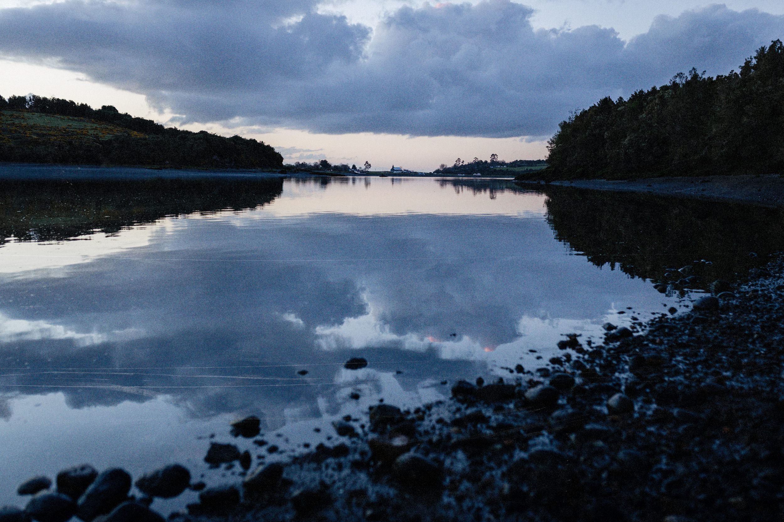 El estero de Apiao en calma, con el cielo reflejado y árboles en la orilla