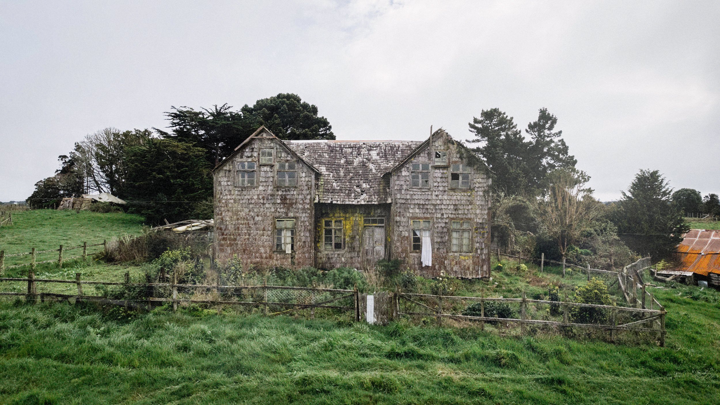 Casa de dos aguas cubierta de tejuelas, rodeada de pasto y árboles, en Chullec